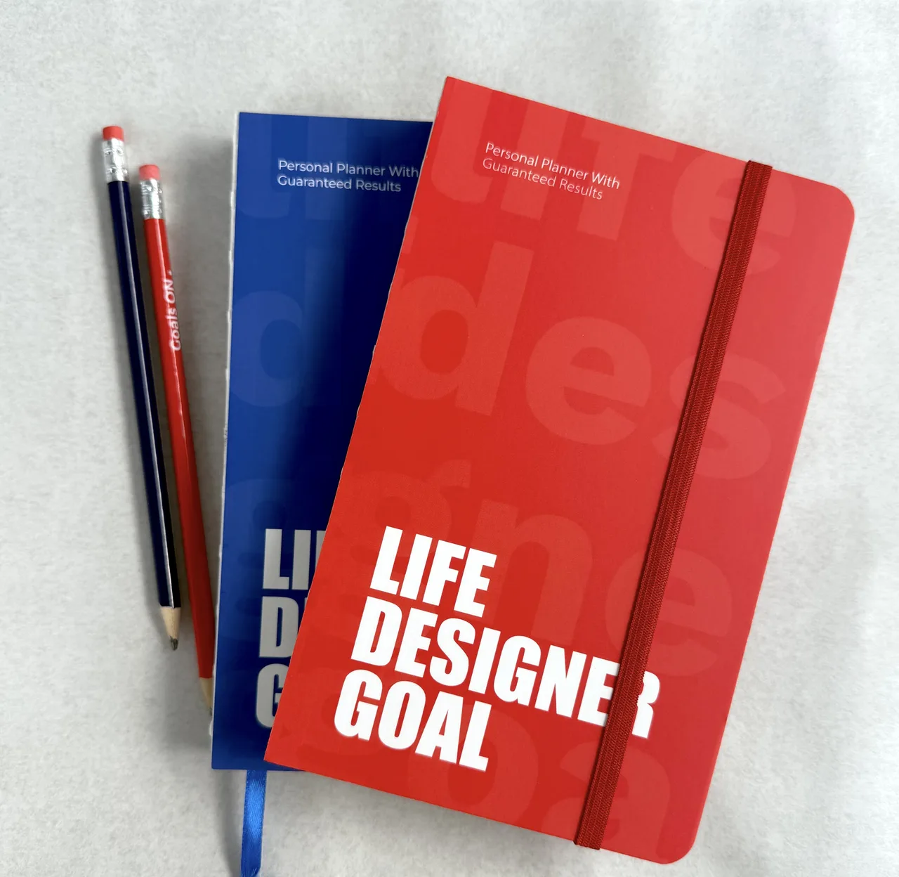 Life Designer GOAL planners in red and blue with pencils